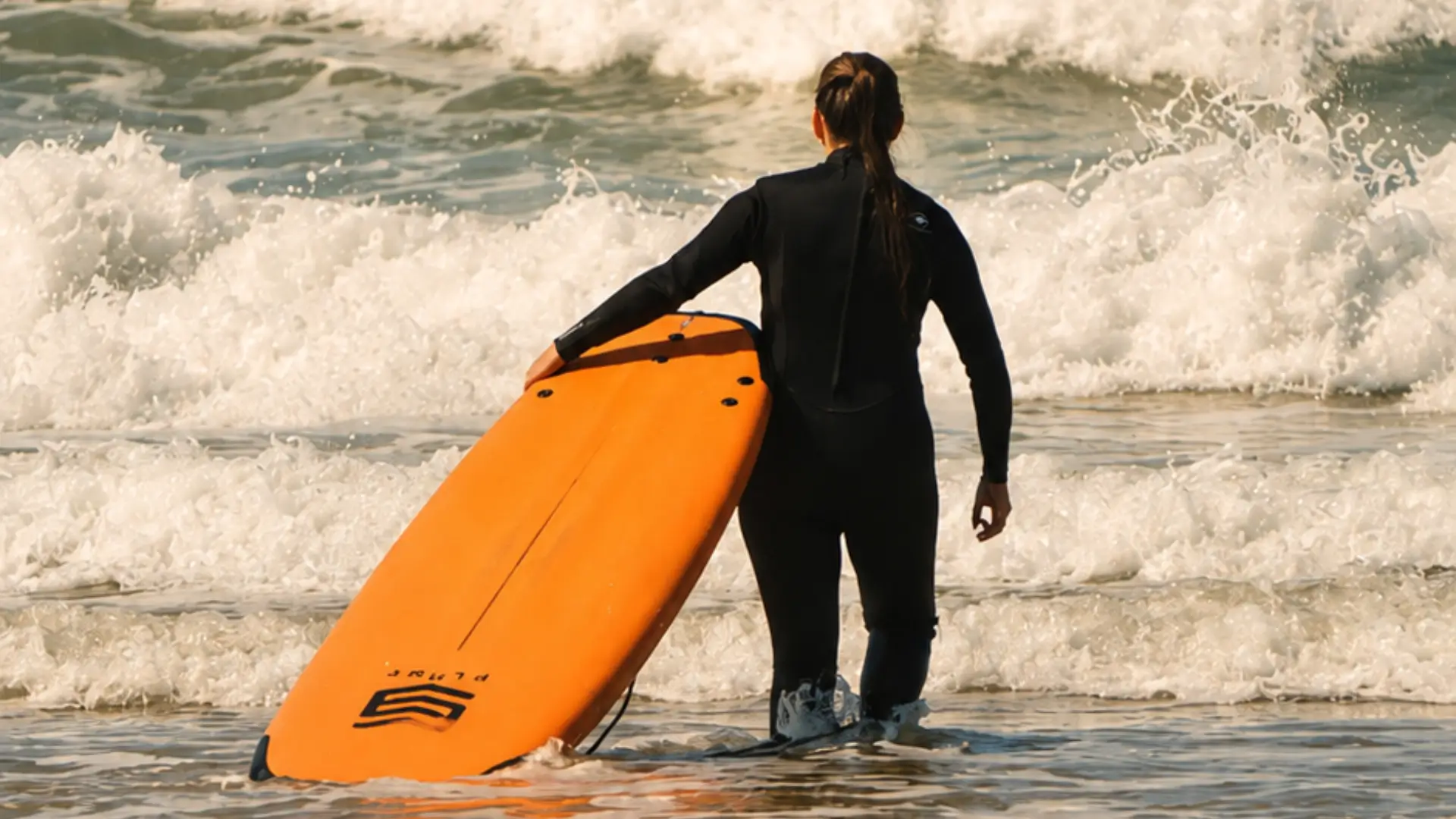 Beginner surfer entering the ocean with a surfboard