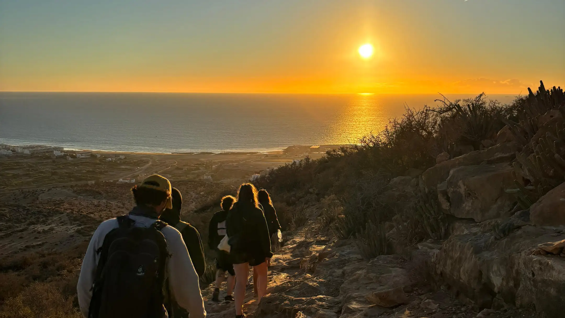 Small group walking along a coastal trail at sunset