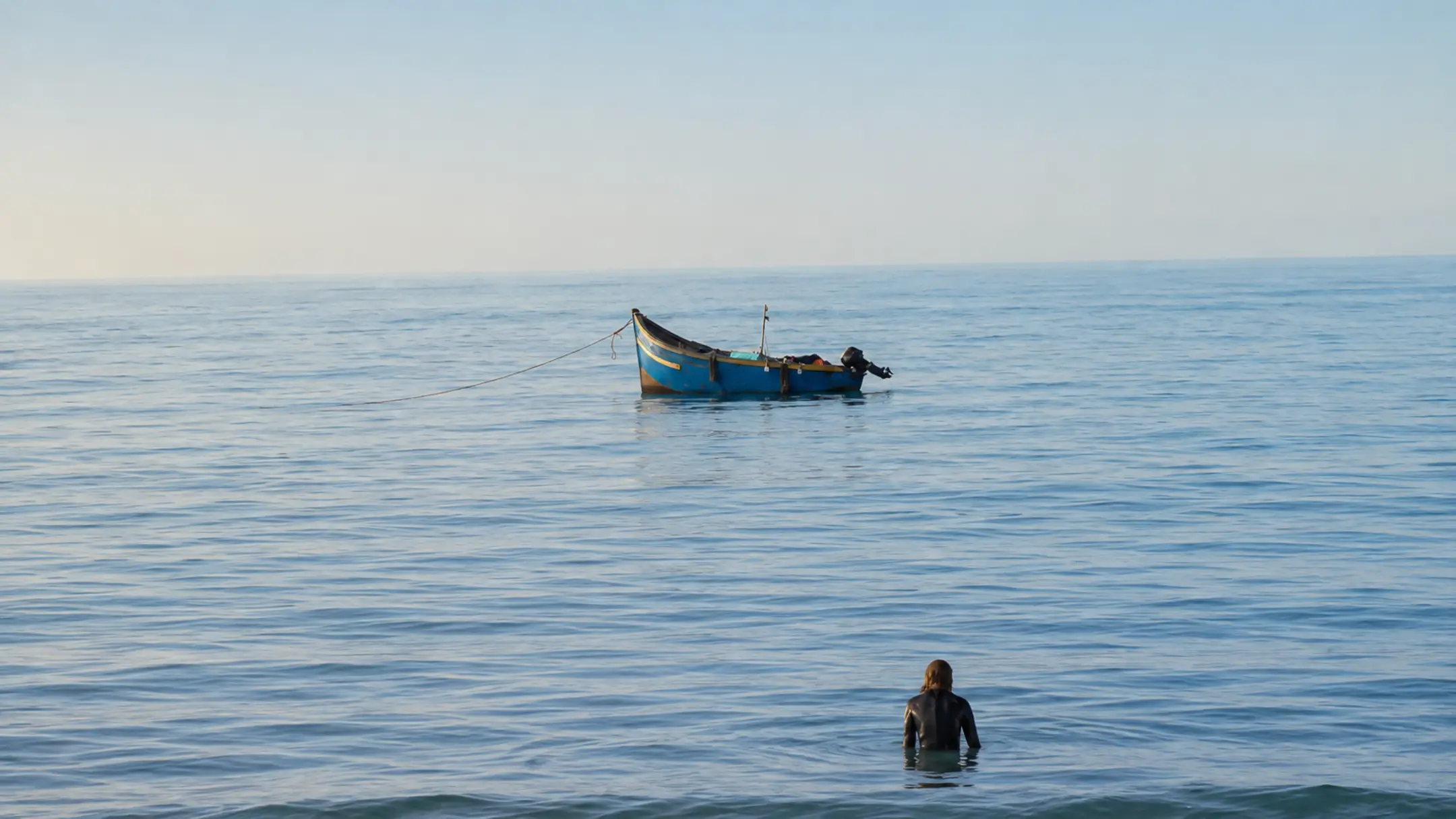 Surfer standing quietly in the Atlantic Ocean with a small fishing boat on the horizon
