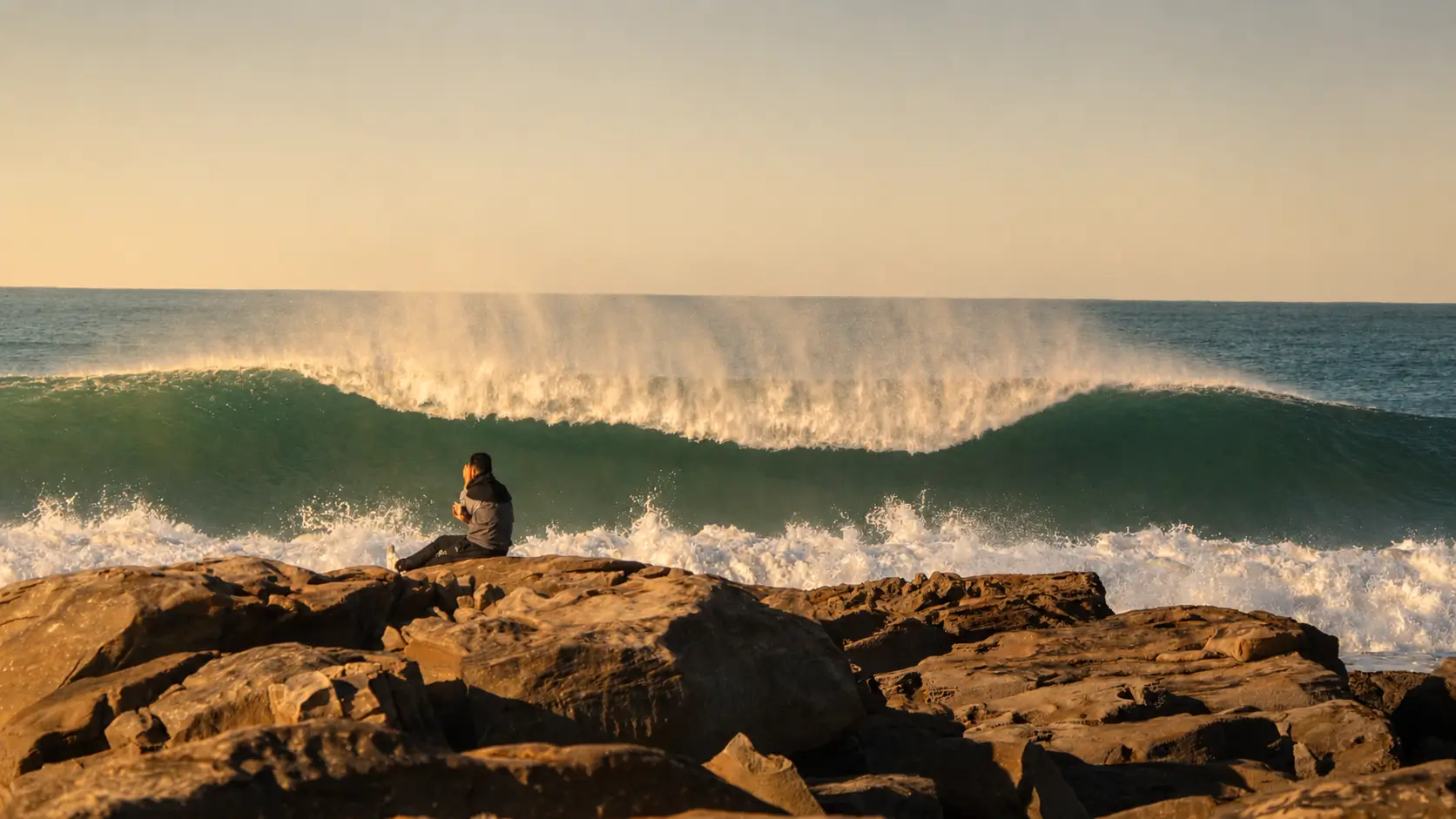 Person sitting on the rocks watching a large Atlantic wave