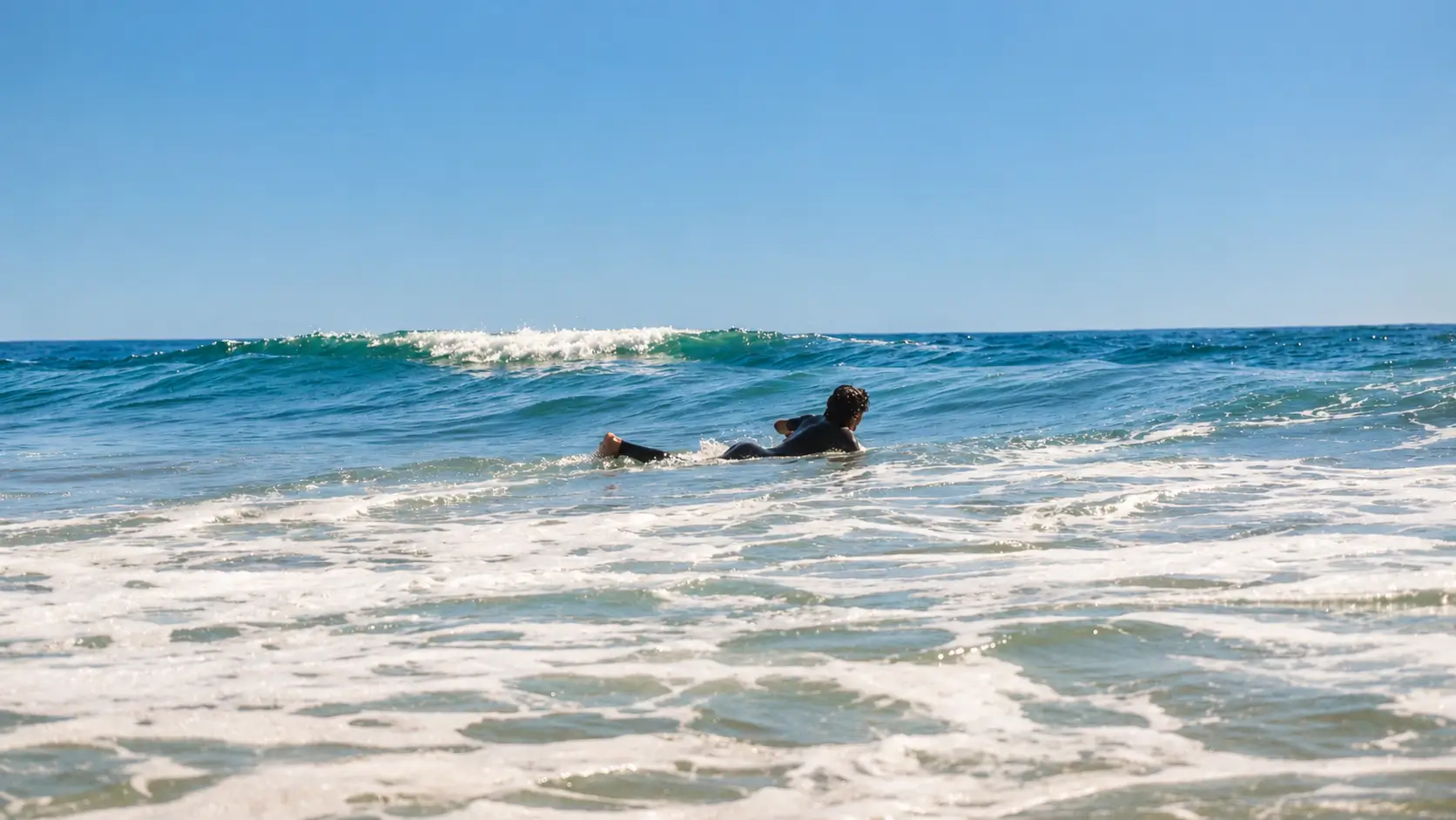 Surfer paddling into the Atlantic Ocean toward an approaching wave