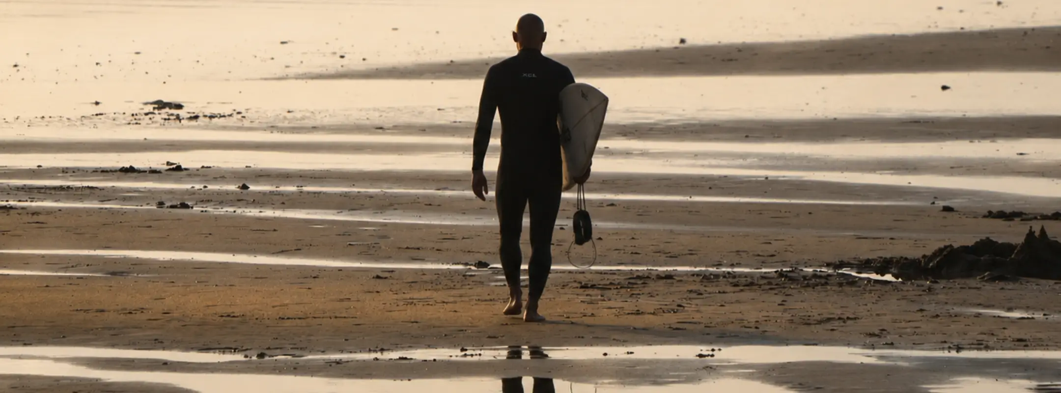 Surfer walking across the beach toward the ocean with a surfboard