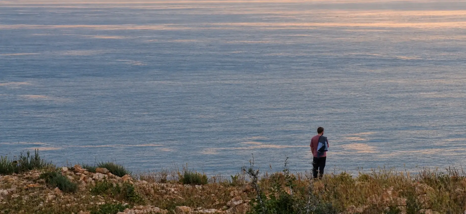 Person standing alone near the ocean at dusk